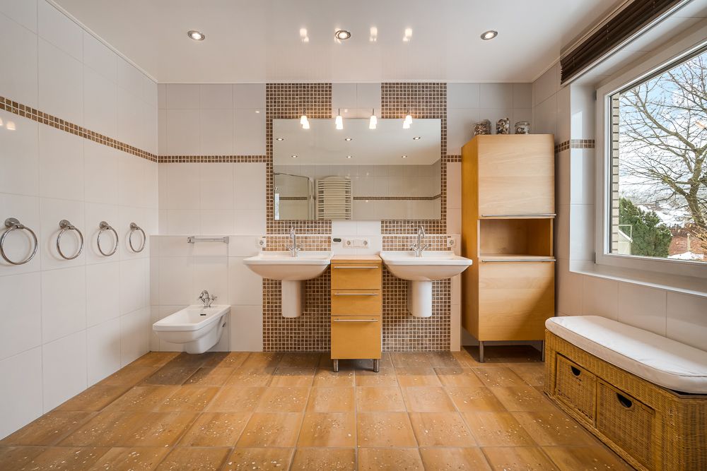 Modernes Badezimmer mit zwei Waschbecken, großem Spiegel, Holzschränken und Fenster.