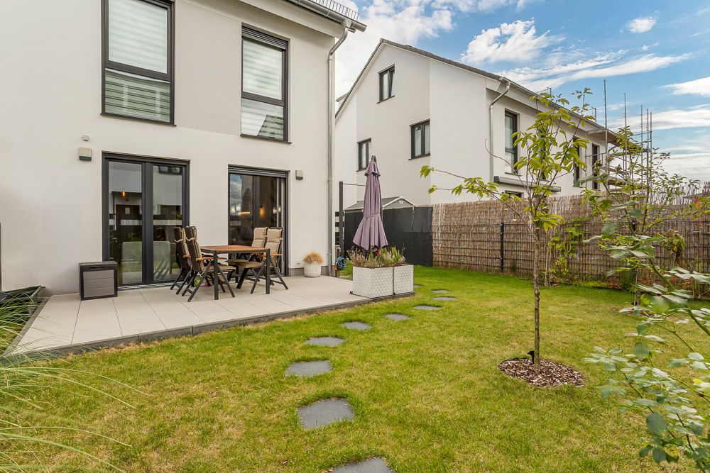 Moderner Garten mit Terrasse, Gartenmöbeln, Sonnenschirm und Rasen mit Trittsteinen.