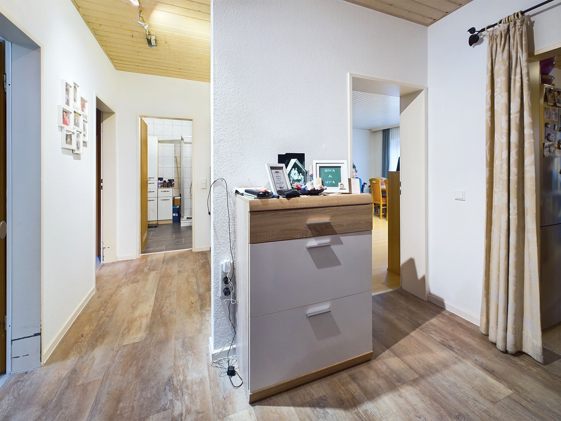 Heller Flur mit Kommode, Holzboden und offenem Zugang zu mehreren Zimmern.