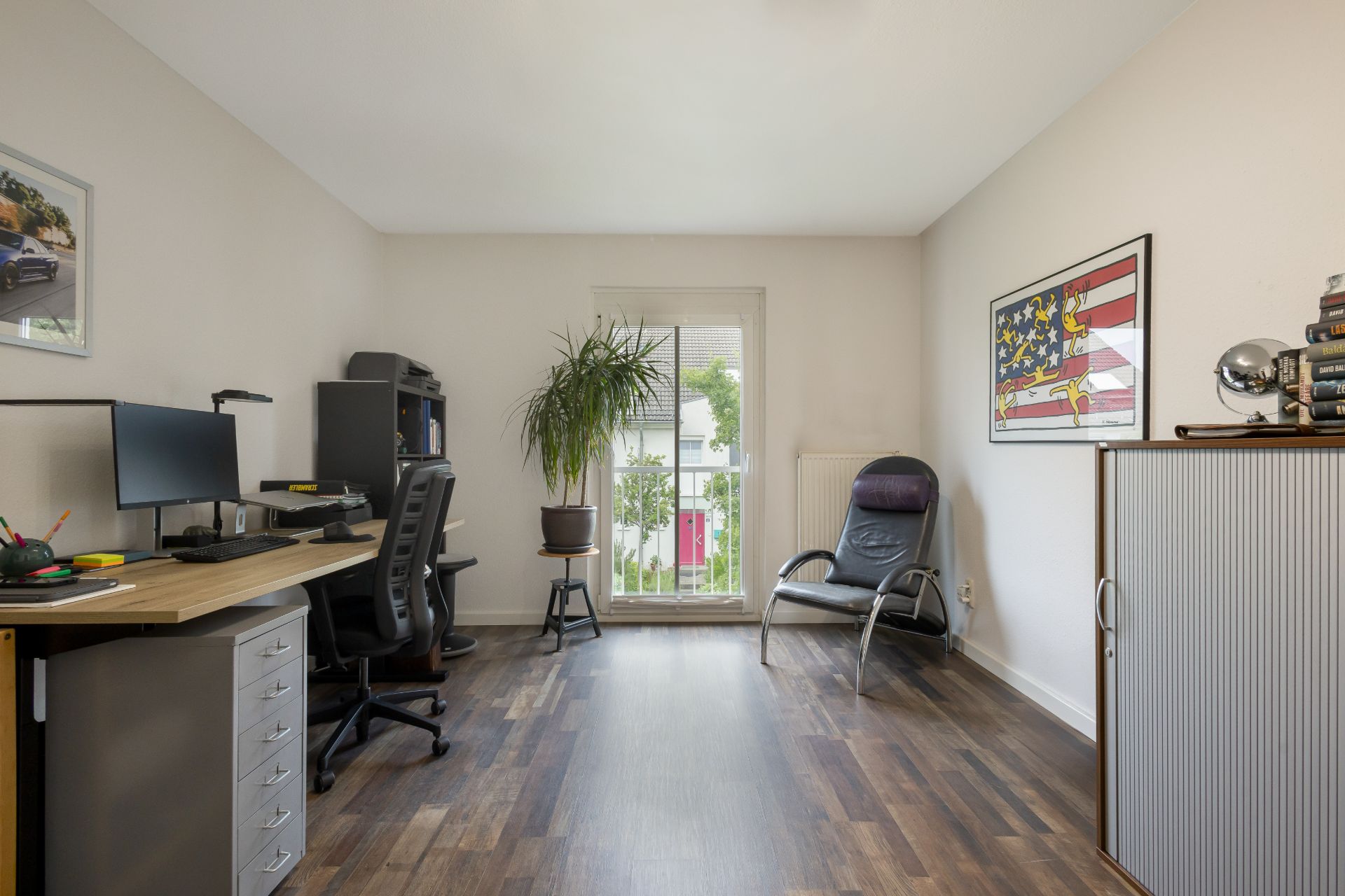 Arbeitszimmer mit Schreibtisch, Stuhl, Pflanze, Sessel und Schrank auf Holzfußboden.