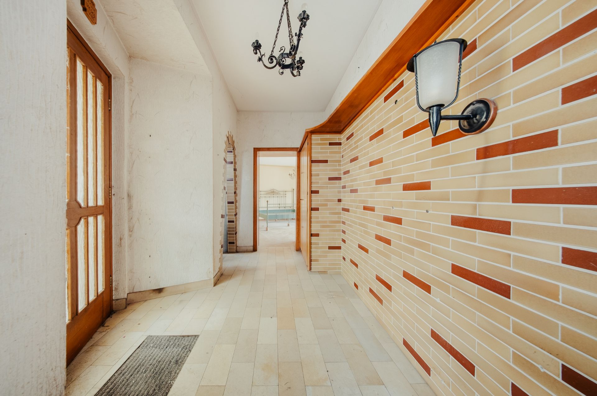 Heller Flur mit gemusterter Wand, Holztür, Wandlampe und Hängelampe.
