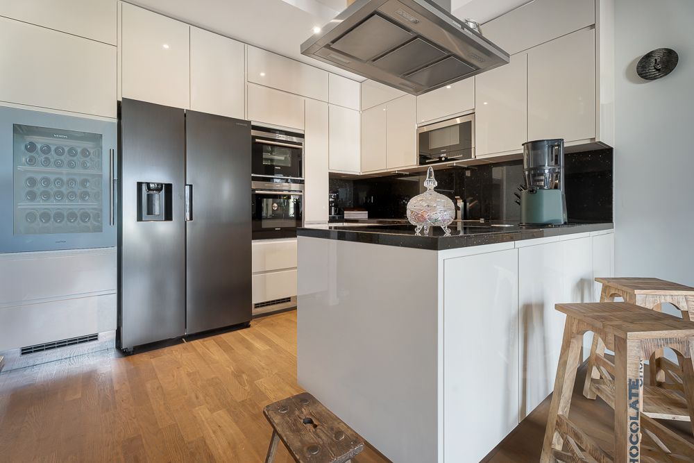 Moderne Küche mit weißen Schränken, dunklem Kühlschrank und Kochinsel mit Hockern.