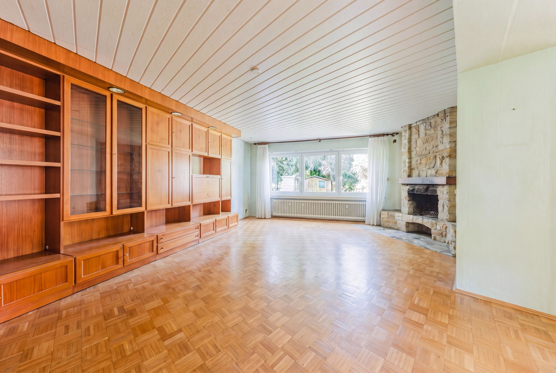 Helles Wohnzimmer mit Holzregalwand, Parkettboden, großem Fenster und Steinkamin.