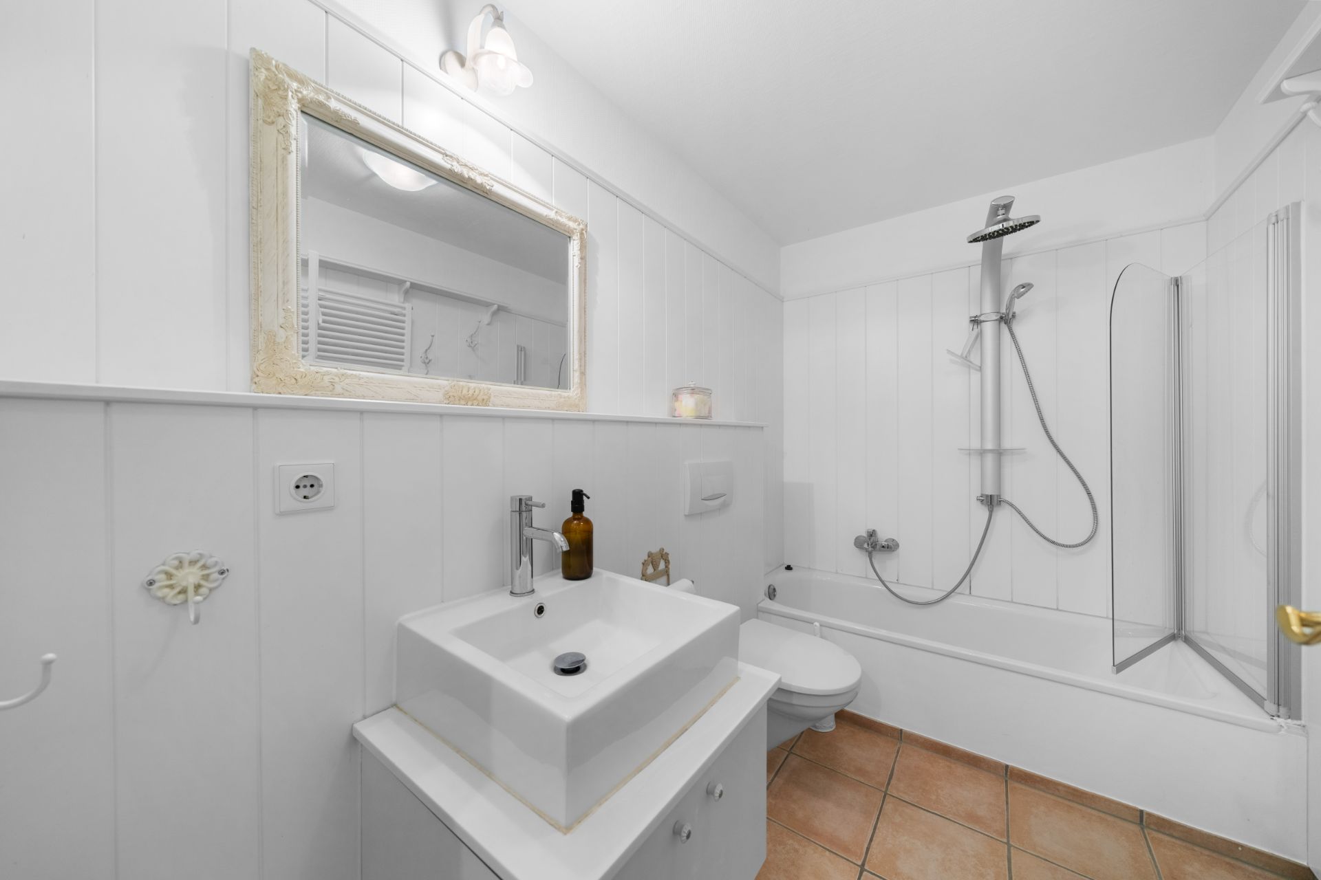 Modernes Badezimmer mit weißem Waschbecken, Spiegel und Badewanne mit Duscharmatur.