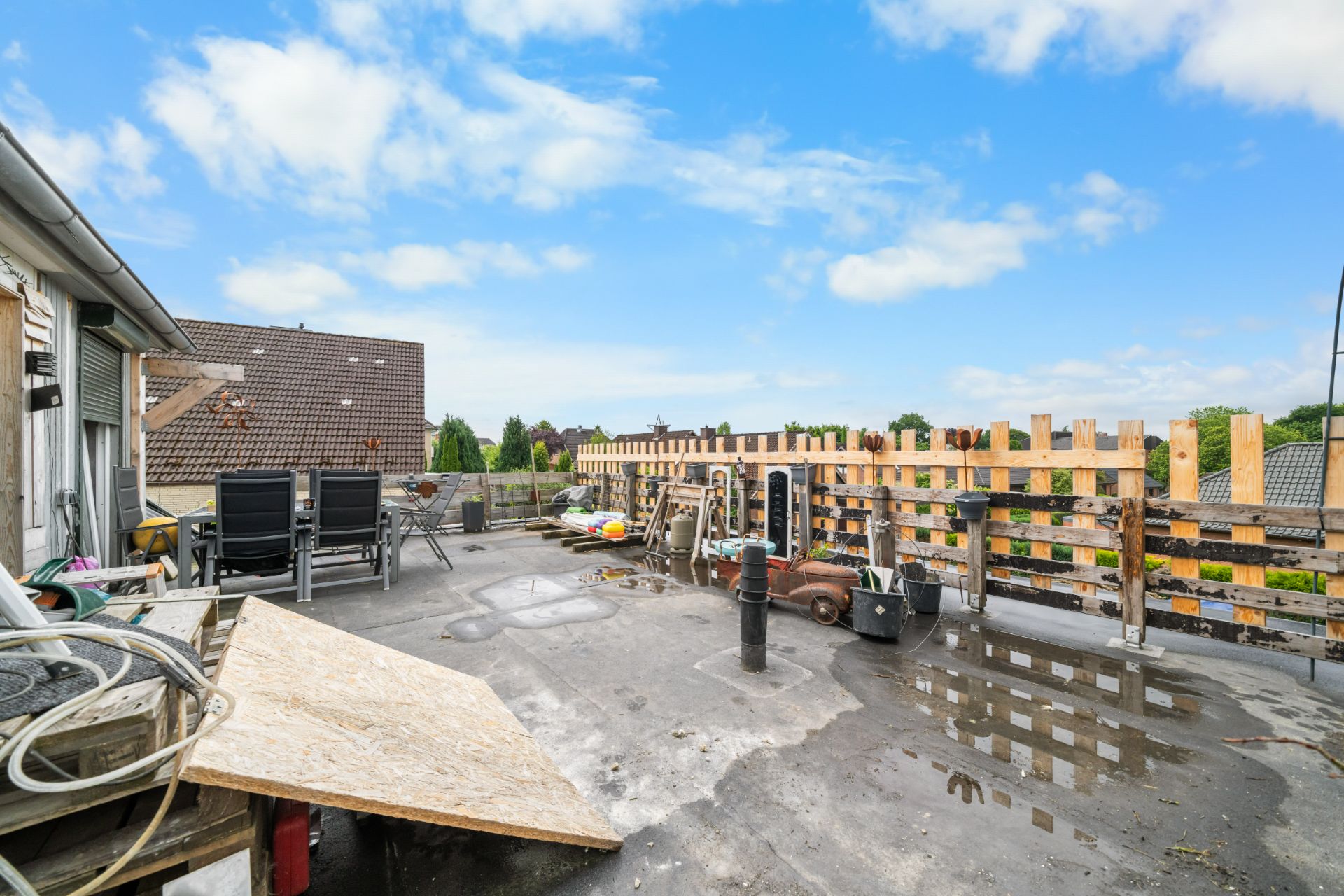 Dachterrasse mit Stühlen, Holzzaun, verschiedenen Gegenständen und Blick auf Nachbarhäuser.