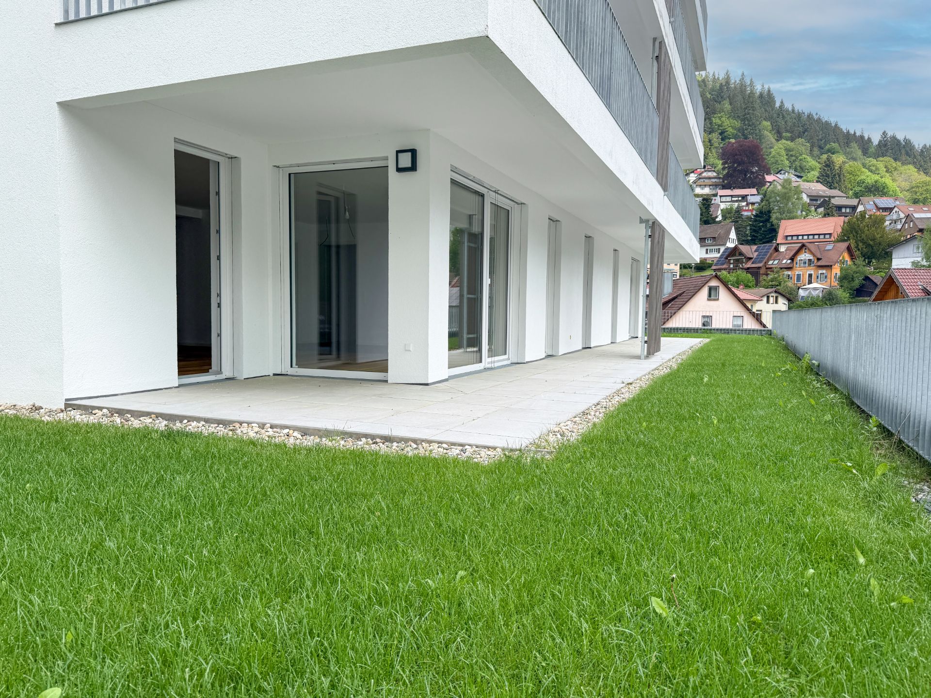 Moderne Terrasse mit Glas-Schiebetüren und Rasenfläche an einem Wohnhaus.