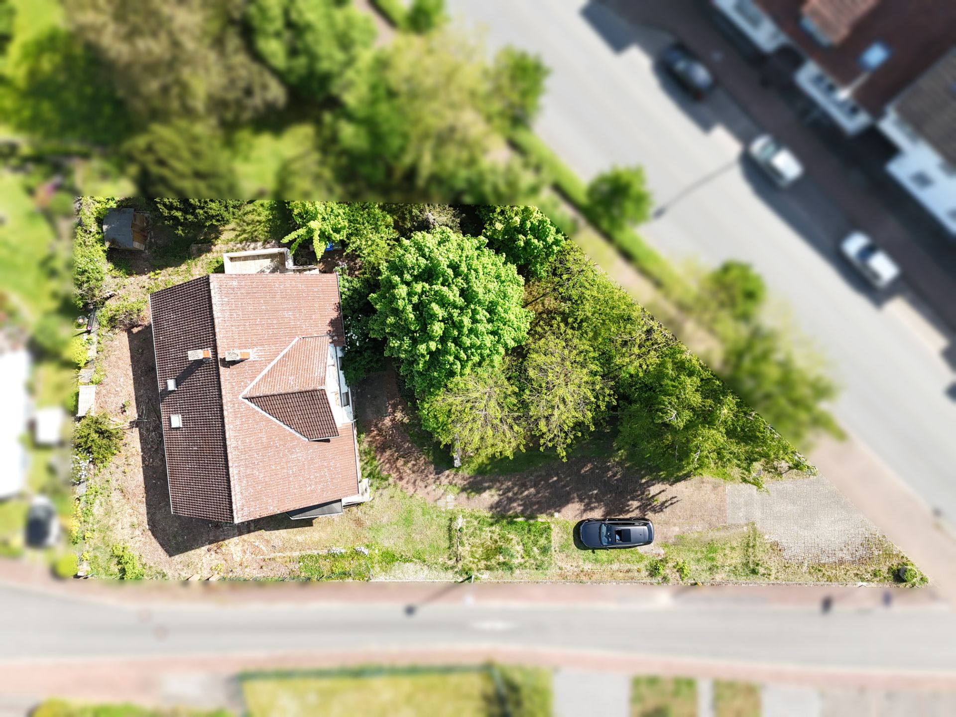 Luftaufnahme eines Hauses mit Garten und geparktem Auto auf einem Grundstück an einer Straße.