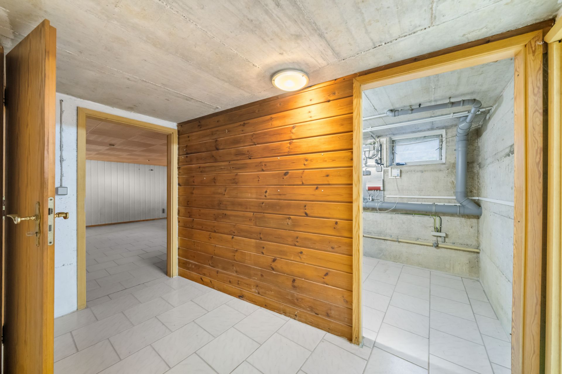 Flur mit Holzverkleidung im Keller, Türen führen zu zwei hellen Räumen mit Fliesenboden.