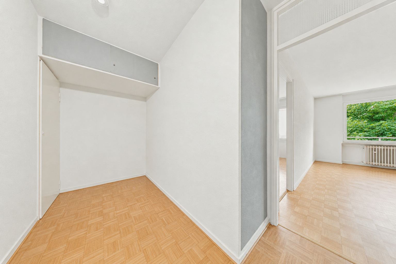 Heller Flur mit Holzboden und Zugang zu einem Zimmer mit großem Fenster.