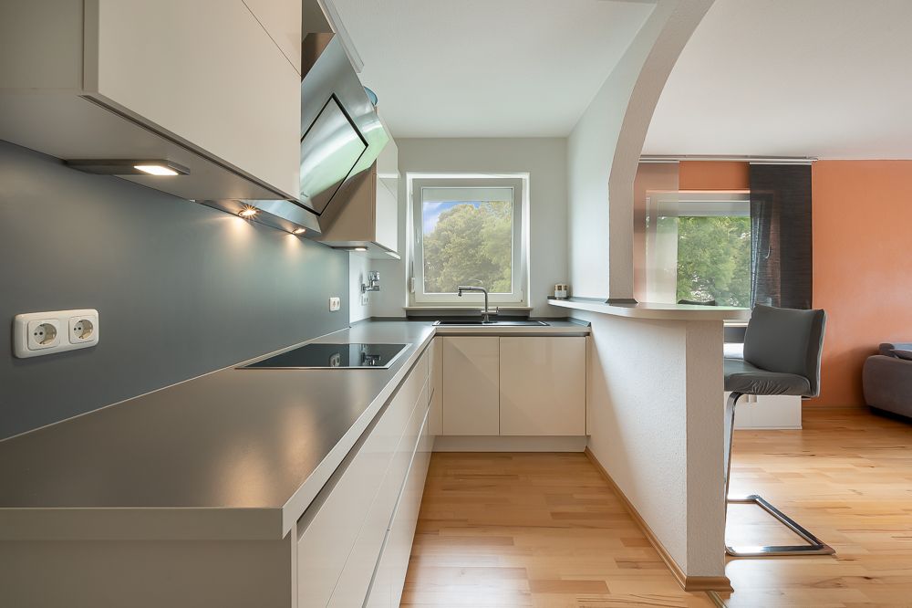 Moderne Einbauküche mit Fenster, Tresen und angrenzendem Wohnbereich mit Parkettboden.
