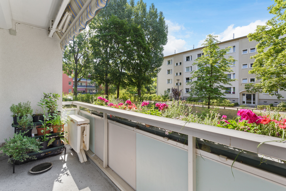 Balkon mit Blumen und Pflanzen, Blick auf grüne Bäume und Wohngebäude im Hintergrund.