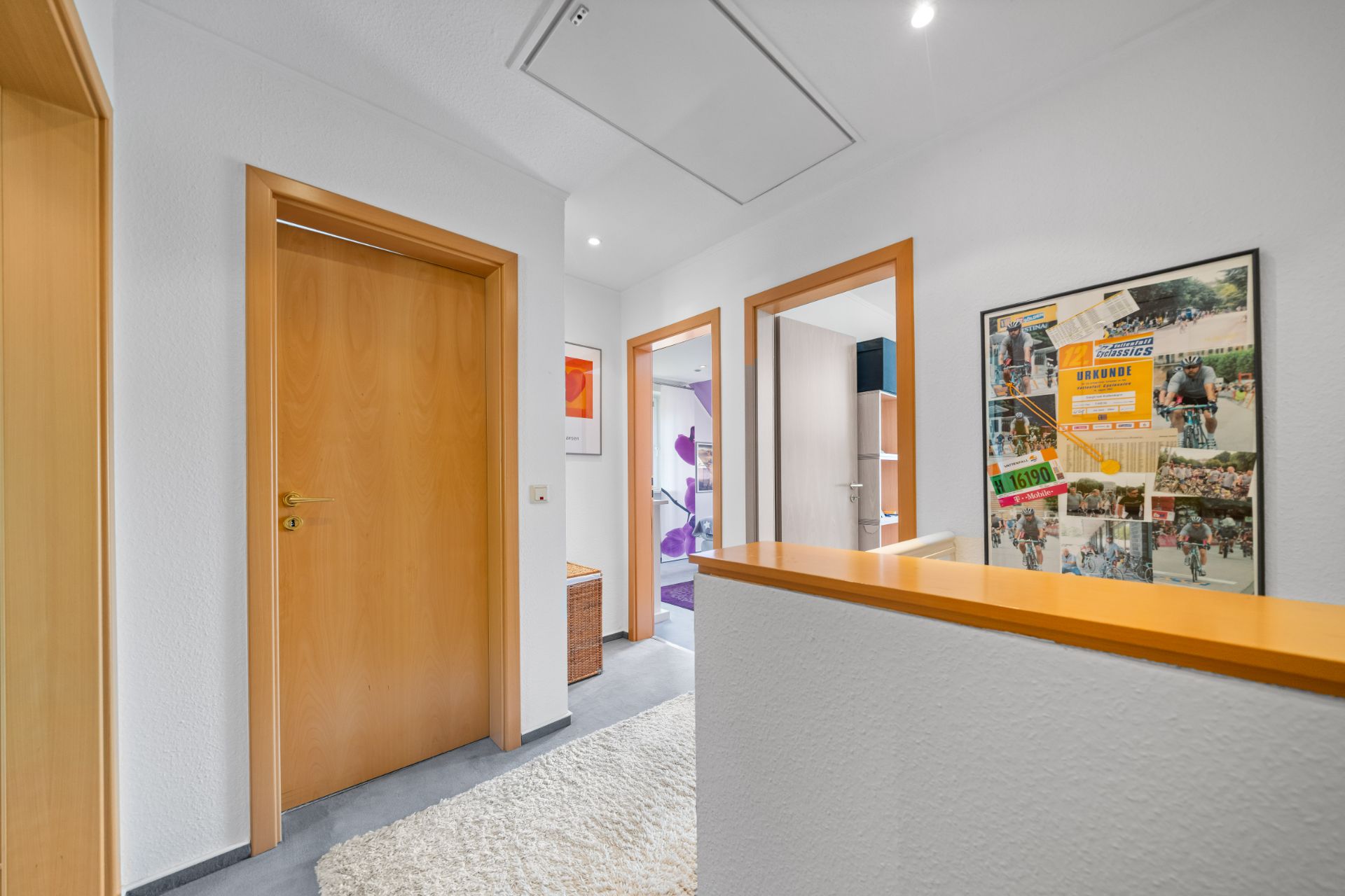Heller Flur mit Holztüren, Teppich und gerahmtem Bild an der Wand.