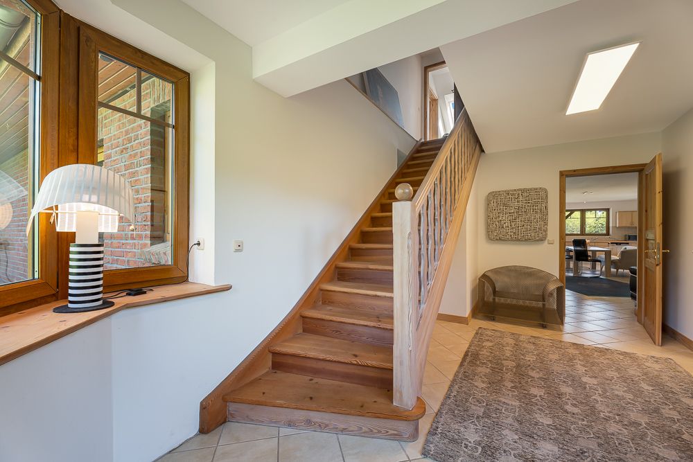 Flur mit Holztreppe, großem Fenster, Teppich und Blick in ein Wohnzimmer.