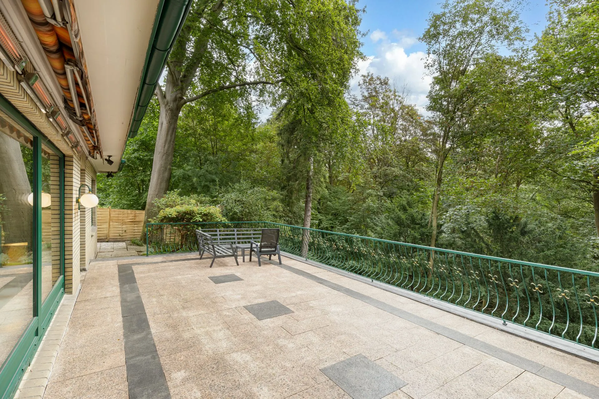 Große Terrasse mit Tisch, Stühlen und Blick auf einen grünen Garten mit vielen Bäumen.