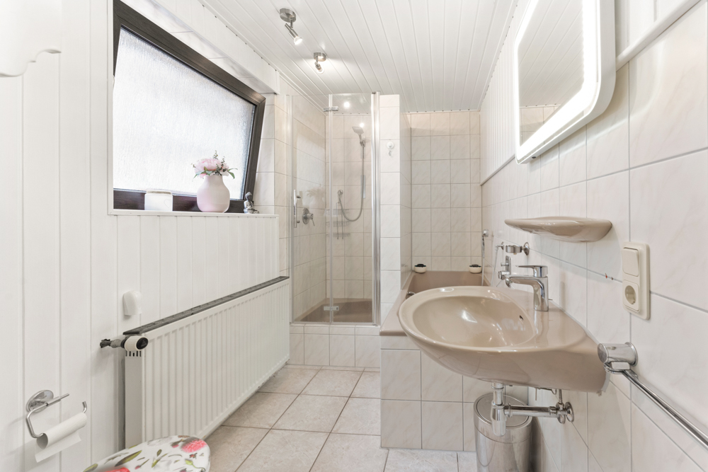 Helles Badezimmer mit Waschbecken, Dusche, Badewanne und großem Fenster.