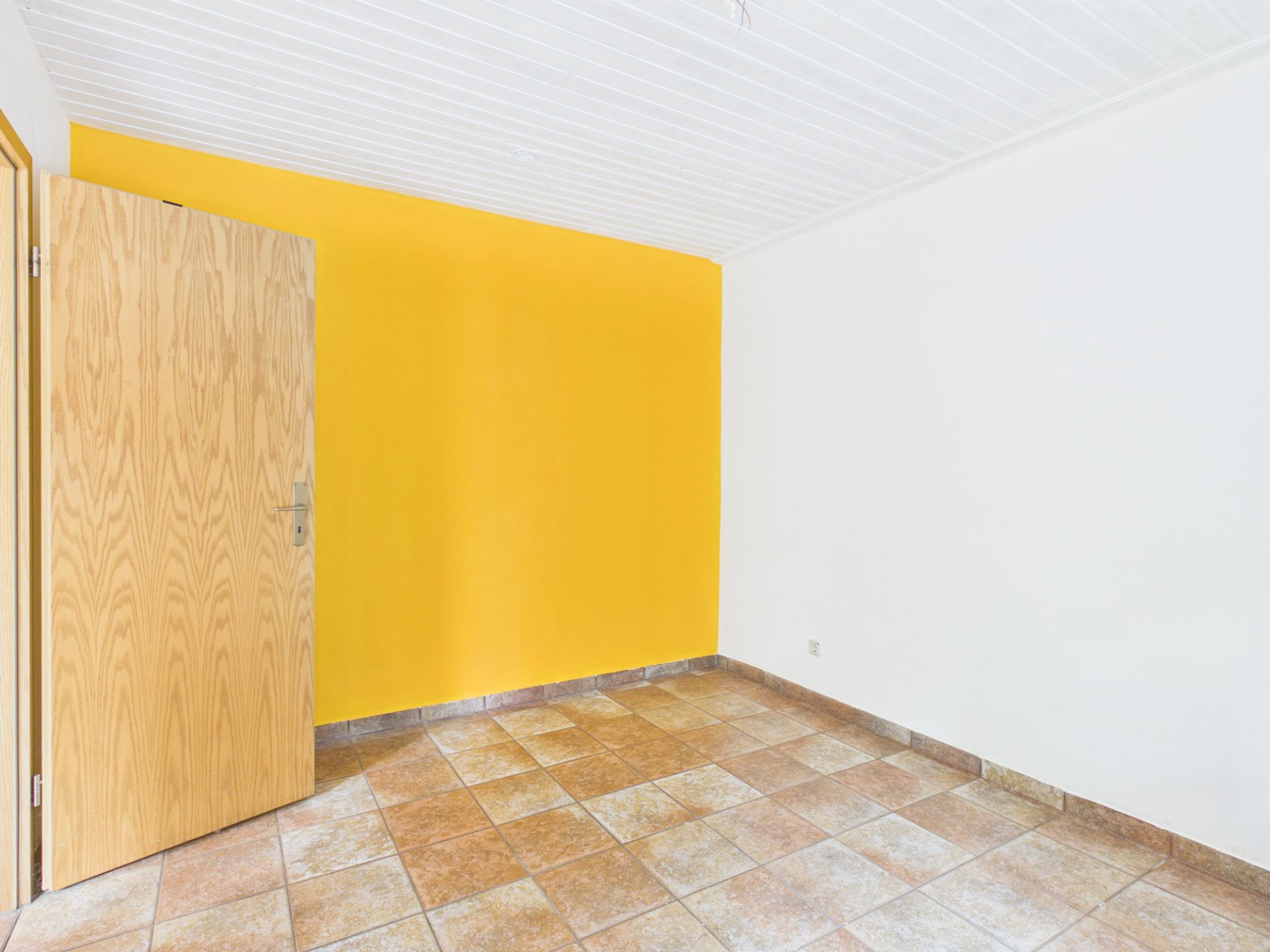 Leerer Raum mit gelber und weißer Wand, Fliesenboden und geöffneter Holztür.