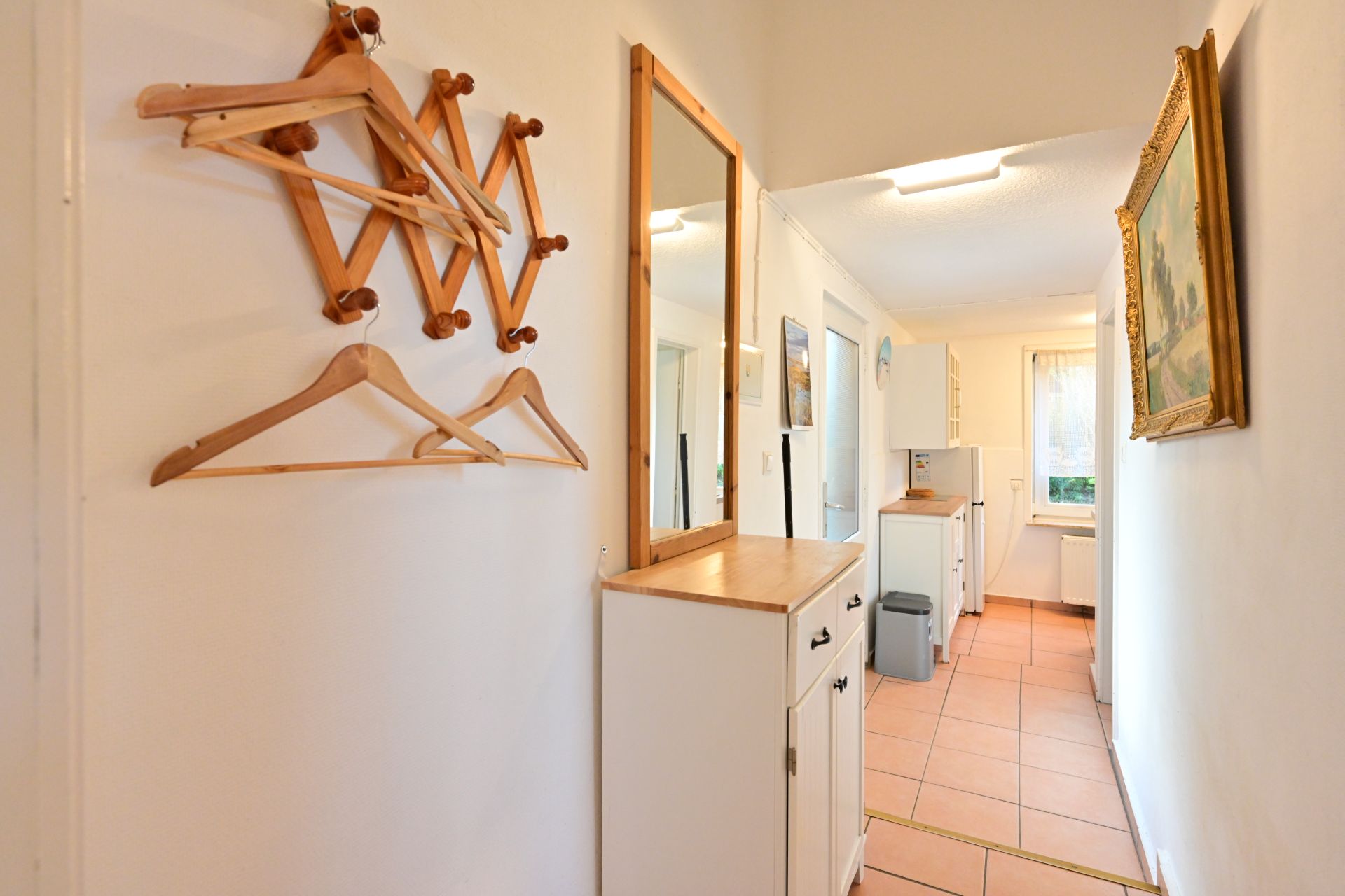 Flur mit Garderobe, Spiegel und Blick in eine helle Küche mit Fliesenboden.