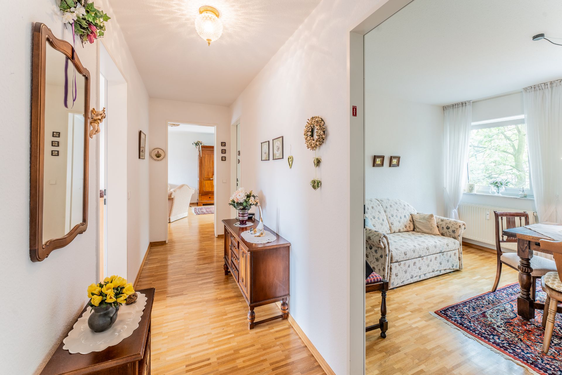 Heller Flur mit Holzboden, Spiegel und Blick auf ein Wohnzimmer mit Sofa und Esstisch.