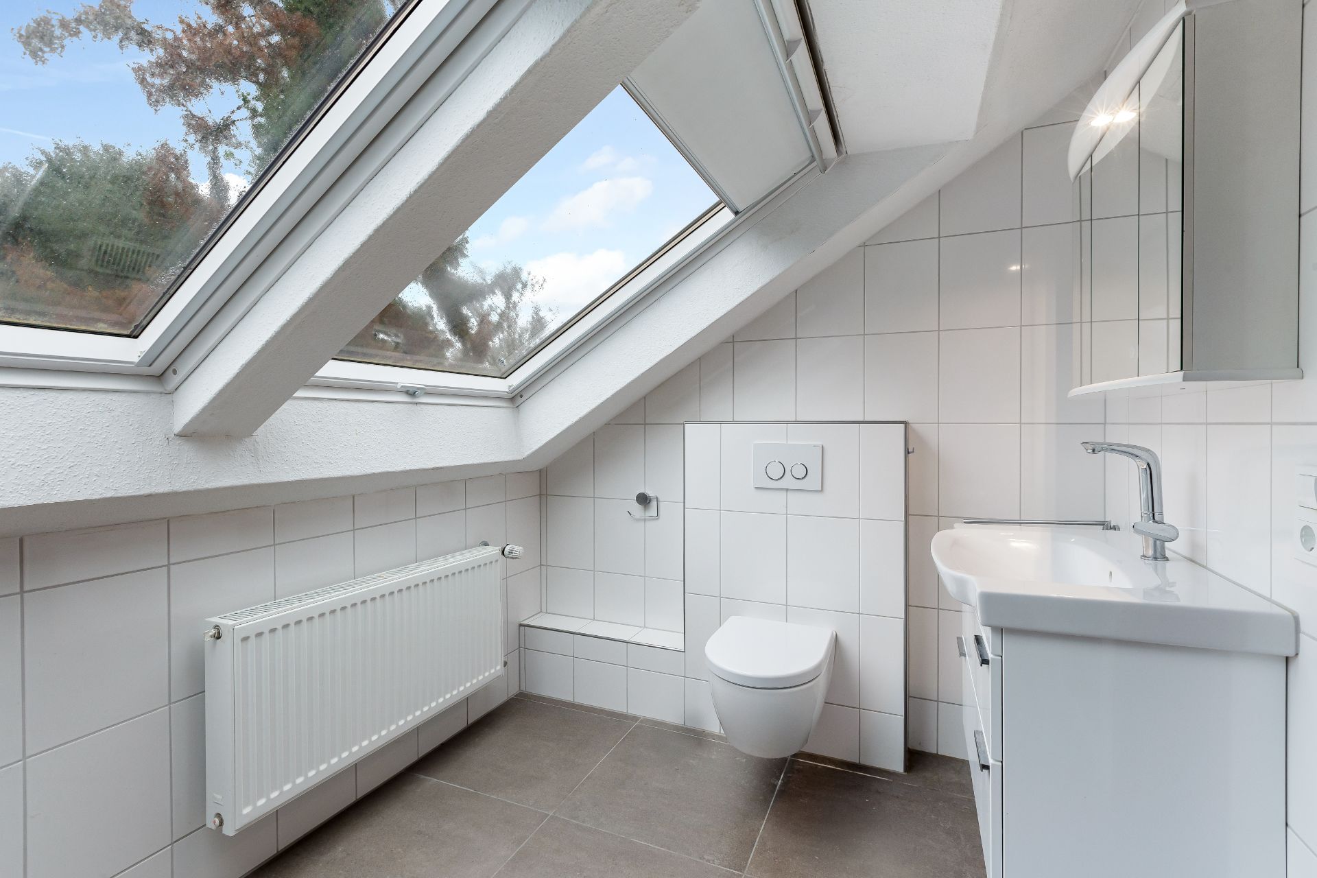 Modernes Badezimmer mit Dachfenster, Hänge-WC, Waschbecken und weißen Fliesen.