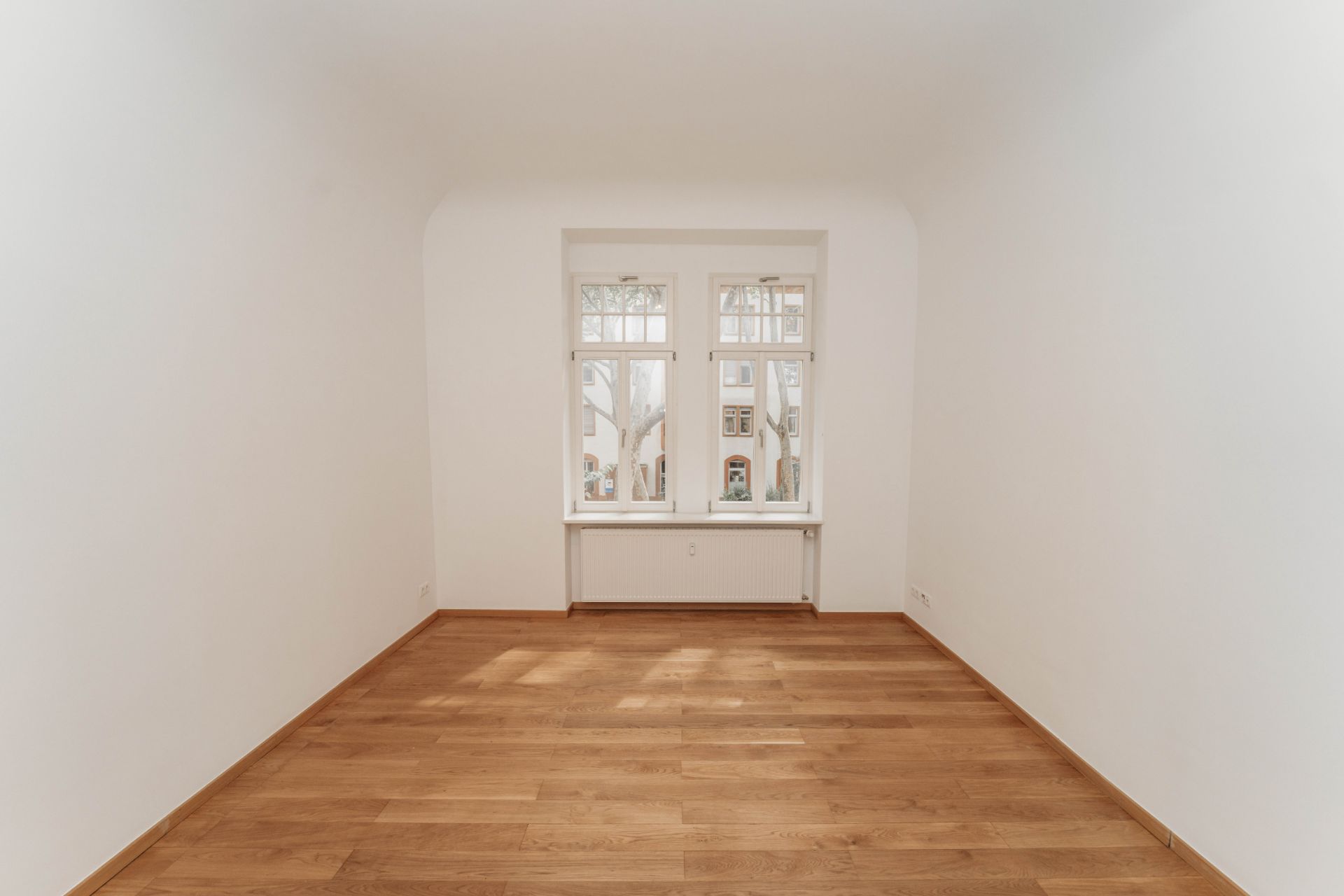 Leerer Raum mit weiß gestrichenen Wänden, Holzfußboden und großem Fenster.