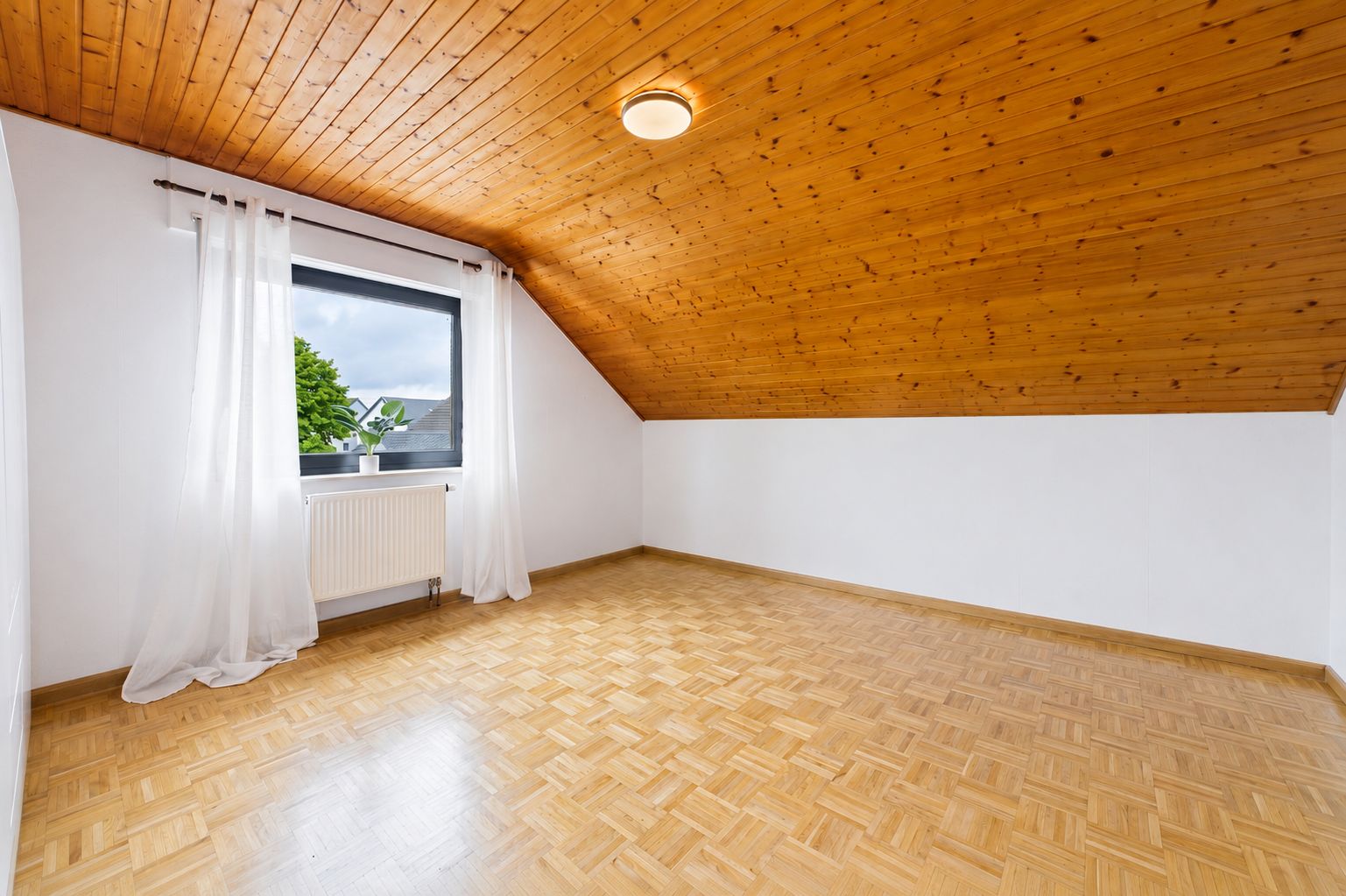 Leerer Raum mit Holzdecke, Parkettboden, Fenster mit weißen Vorhängen und einer Deckenlampe.
