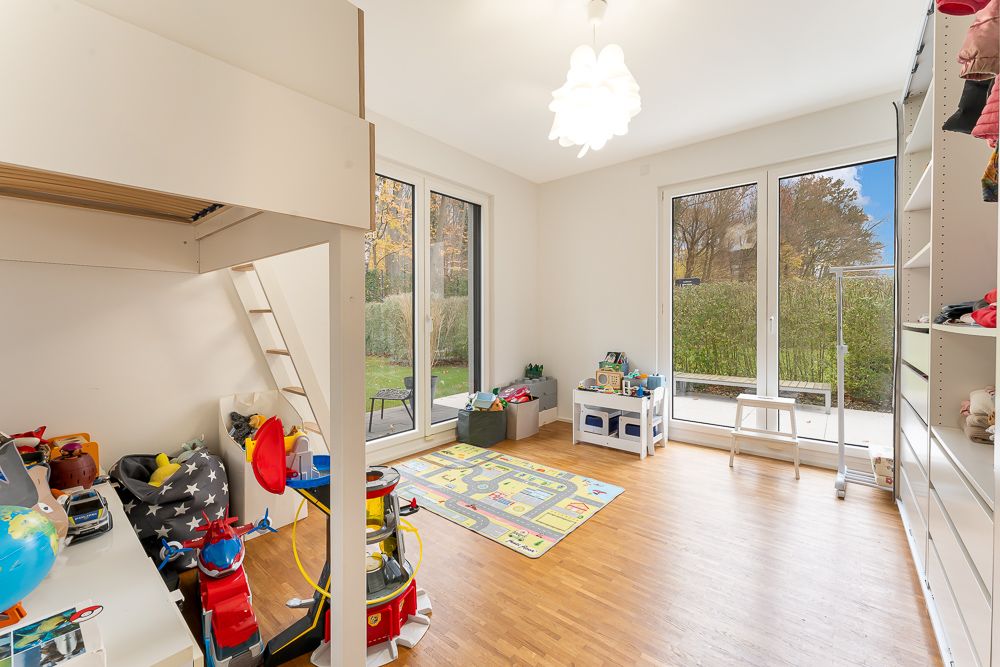 Helles Kinderzimmer mit Hochbett, Spielzeug, Regal und großen Fenstern zum Garten.