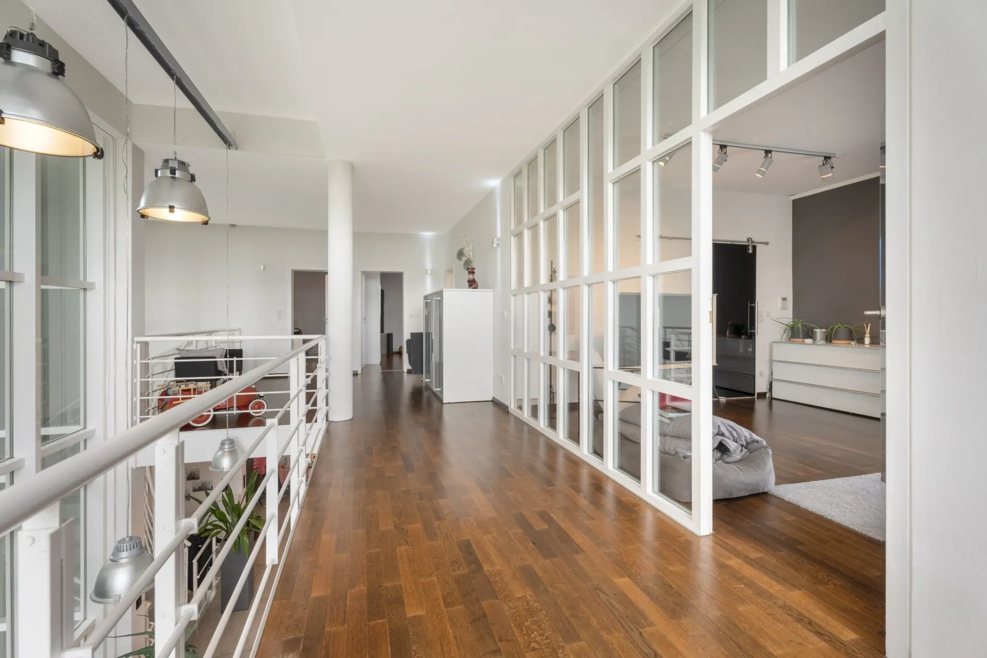 Moderner Flur mit Holzboden, Glaswand und Blick in ein angrenzendes Wohnzimmer.