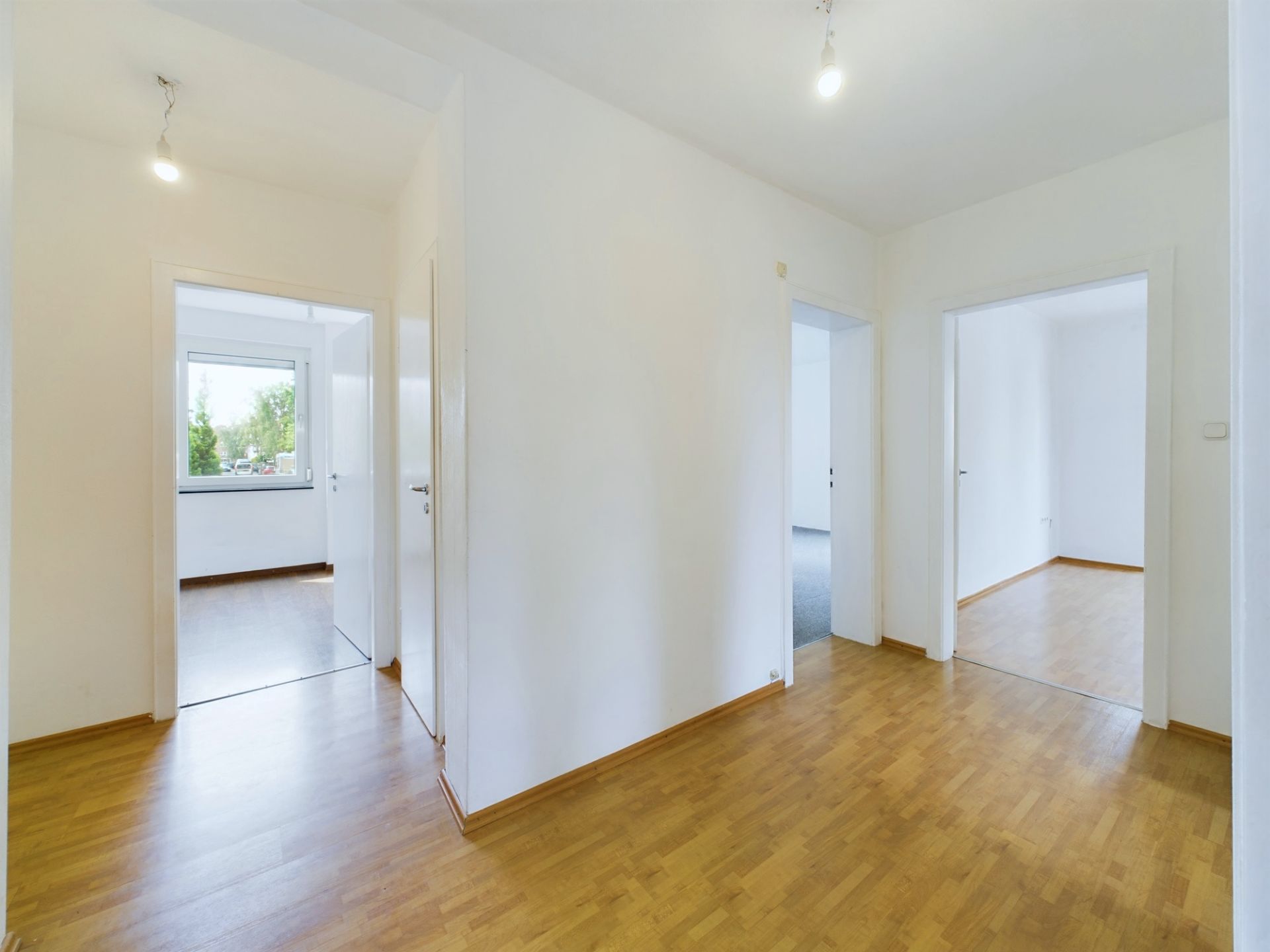 Heller Flur mit Holzboden und Türen zu drei Zimmern, ein Fenster im Hintergrund.