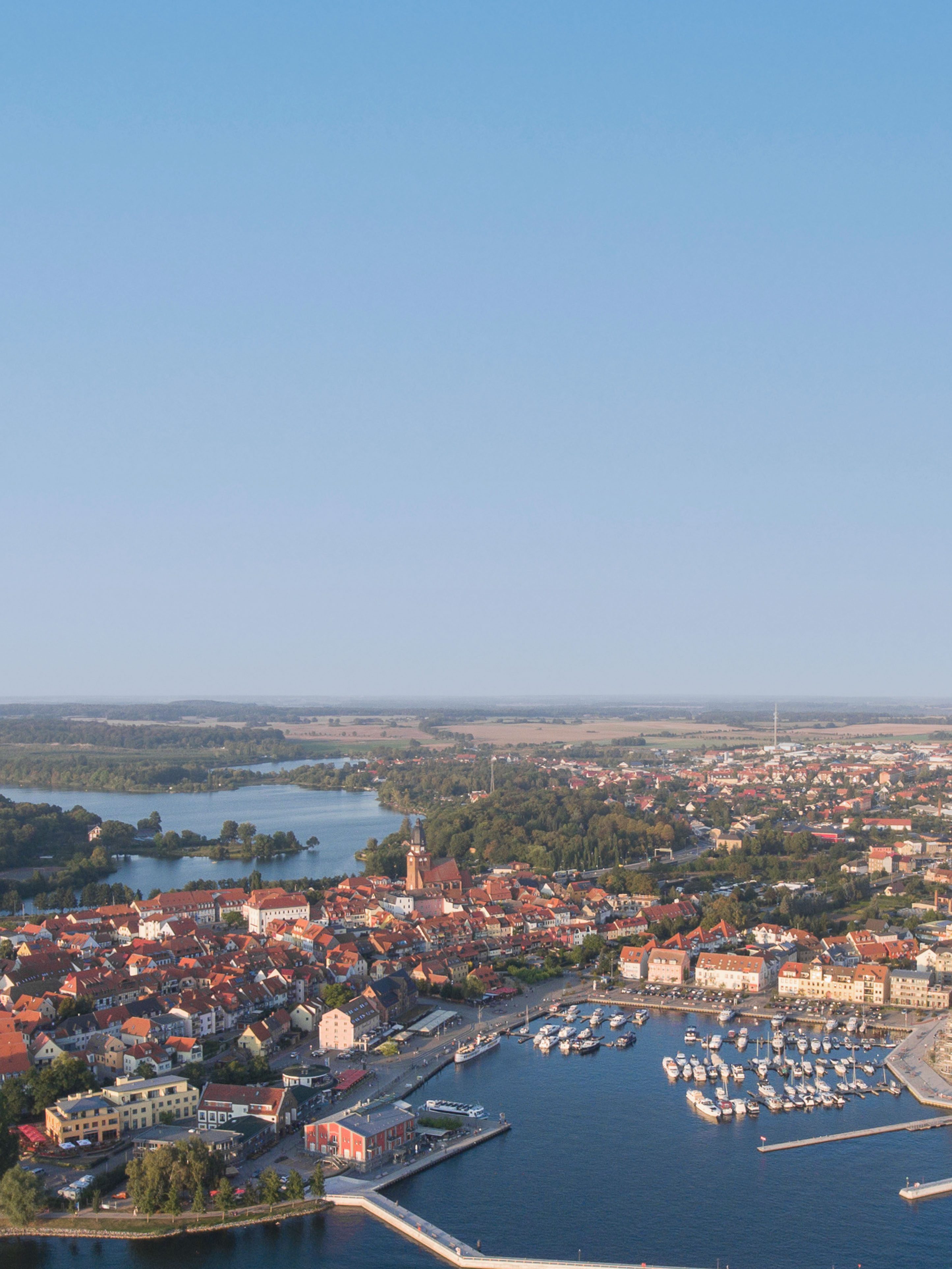 Luftaufnahme einer Stadt mit Hafen, vielen Booten und roten Dächern am Wasser.