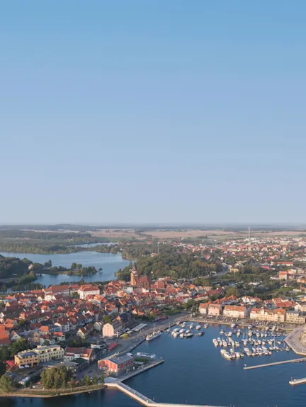 Luftaufnahme einer Stadt mit Hafen, vielen Booten und roten Dächern am Wasser.