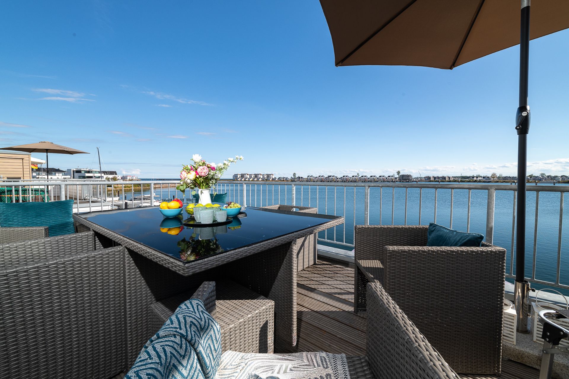Terrasse mit Sitzgruppe, Tisch, Blumen und Blick auf das Wasser.