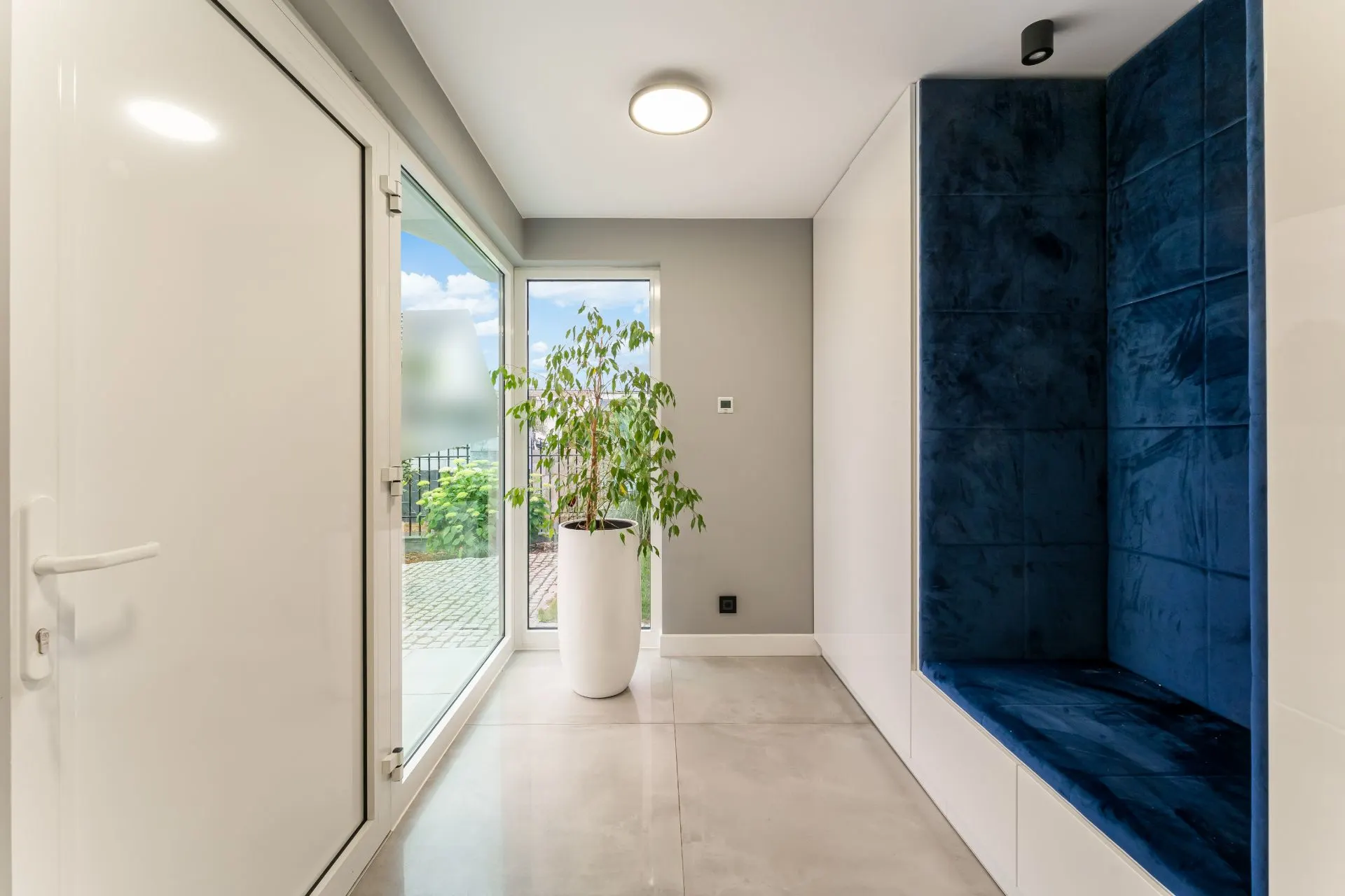 Moderner Flur mit großer Glastür, weißem Blumentopf und blauer Sitznische.