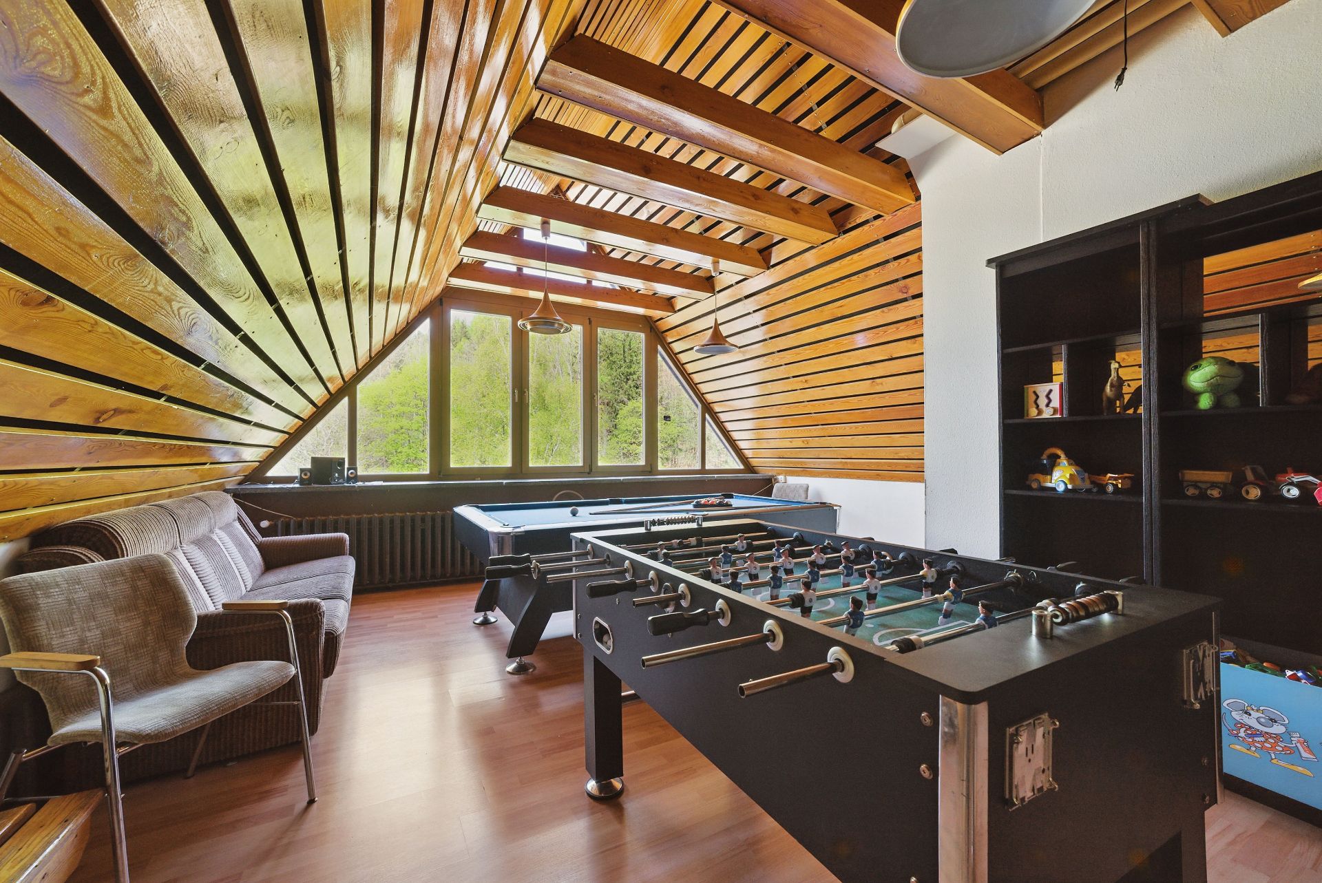 Wohnzimmer mit Tischfußball, Sofa, Regal und großem Fenster, Holzwände und -decke.