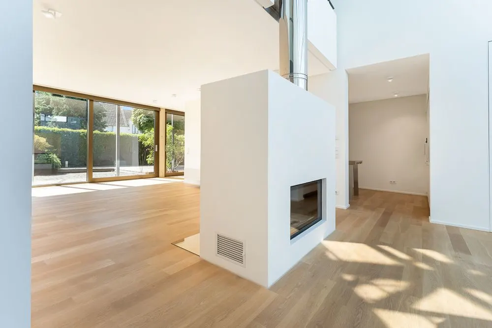 Helles Wohnzimmer mit Holzboden, Kamin und großen Fenstern zum Garten.