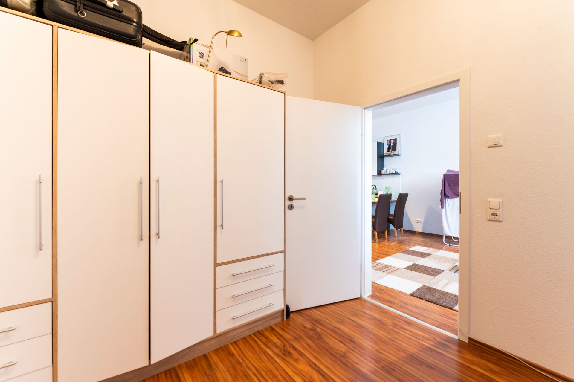 Offene Tür zu einem Zimmer mit weißen Einbauschränken und Holzboden, dahinter ein Essbereich.