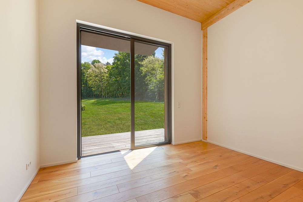 Heller Raum mit Holzfußboden und großer Glas-Schiebetür zu einem Garten.