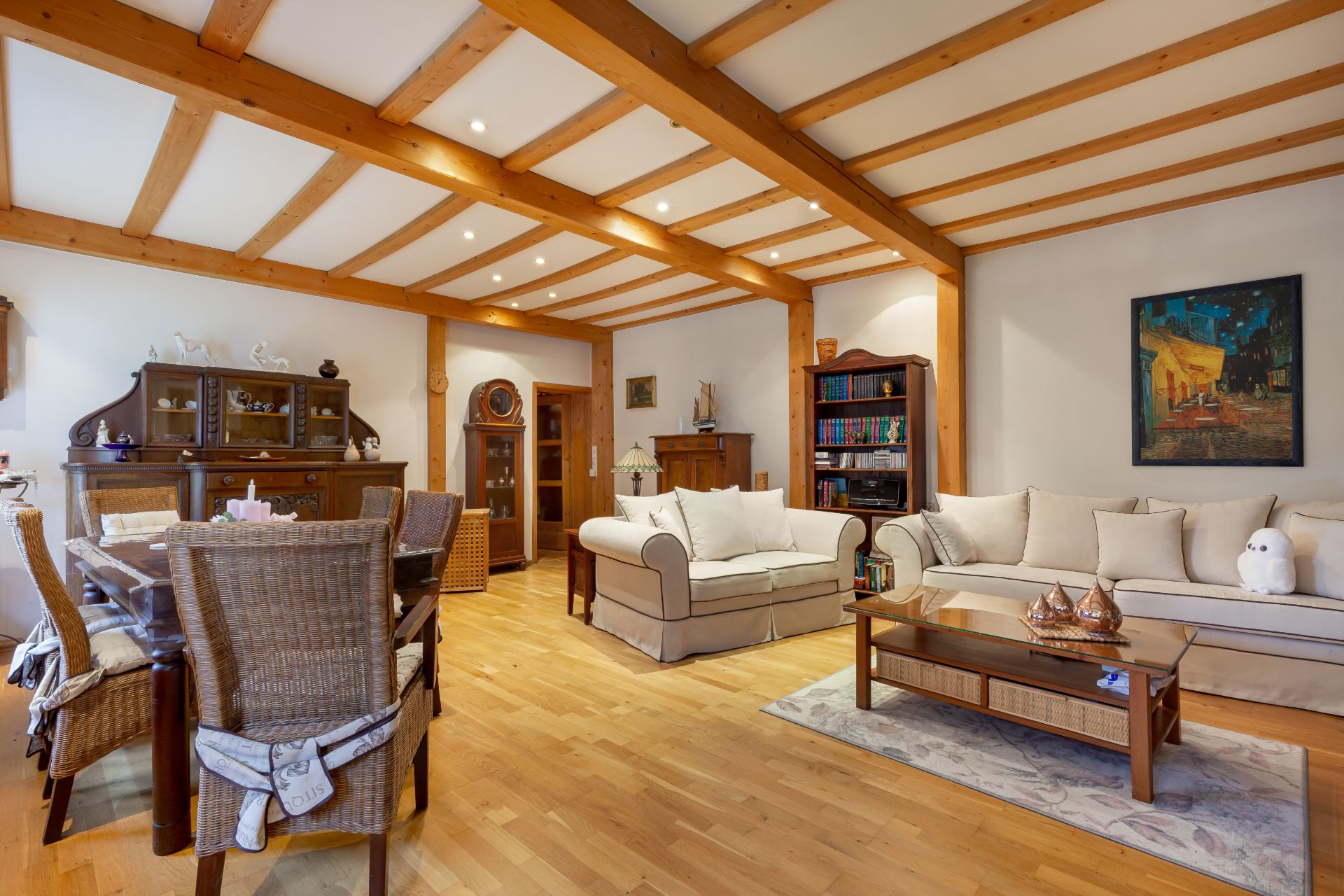 Gemütliches Wohnzimmer mit Holzbalkendecke, Sofas, Esstisch und Bücherregal.