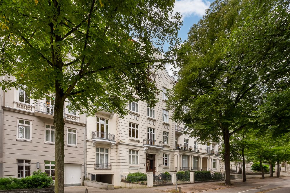 Mehrstöckiges Wohnhaus mit Balkonen, großen Fenstern und Bäumen an einer ruhigen Straße.