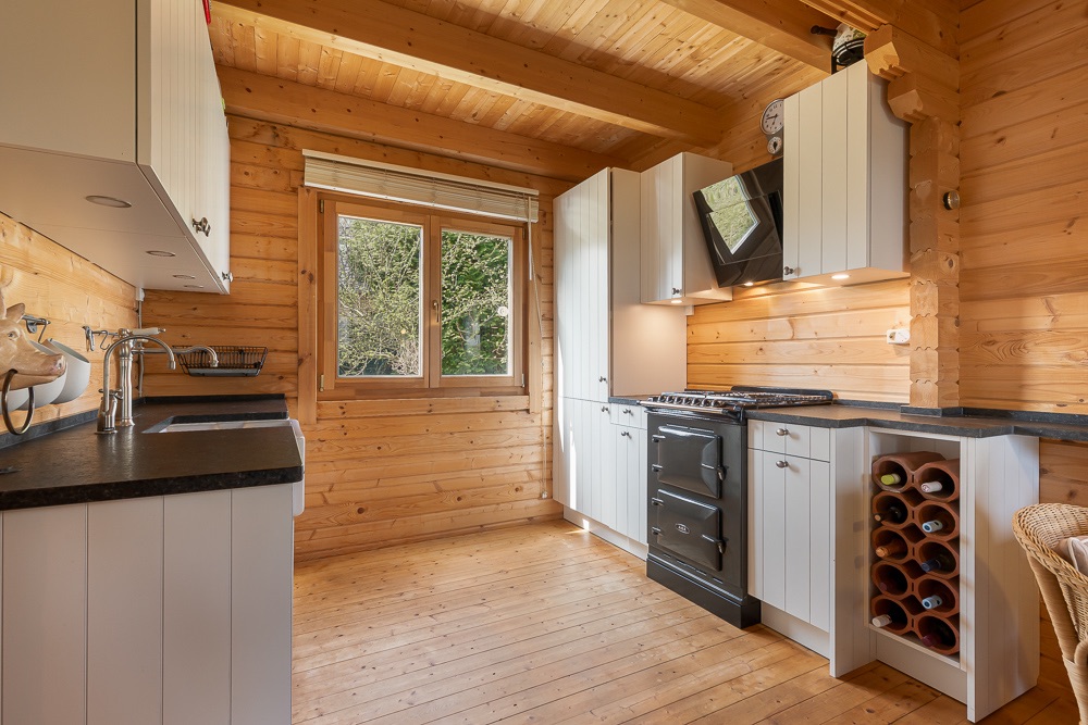 Helle Holzküche mit Fenster, weißen Schränken, Herd und Weinregal.