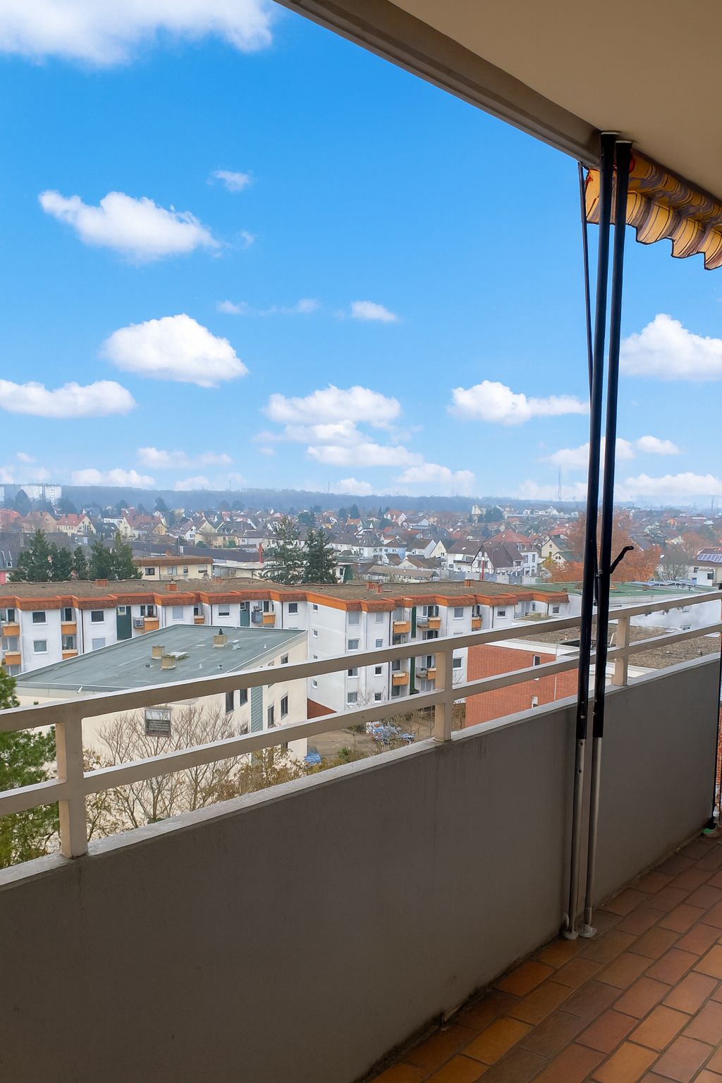 Balkon mit Blick auf Wohnhäuser und blauen Himmel mit wenigen Wolken.