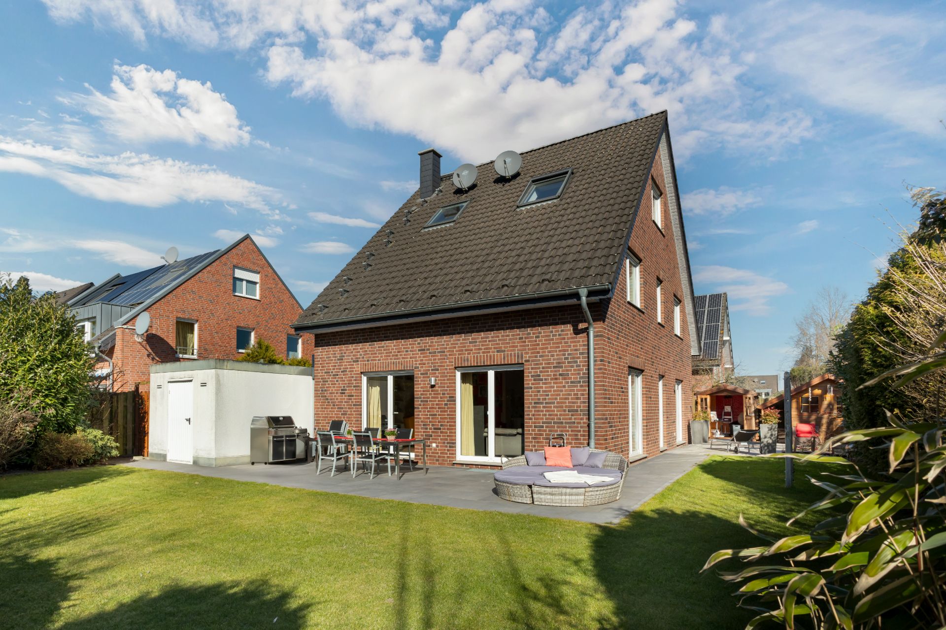 Backsteinhaus mit Terrasse, Gartenmöbeln und großem Rasen im Hinterhof bei sonnigem Wetter.