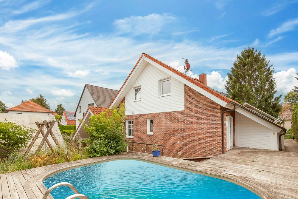 Backsteinhaus mit rotem Dach und Pool im Garten, daneben eine Holzschaukel.