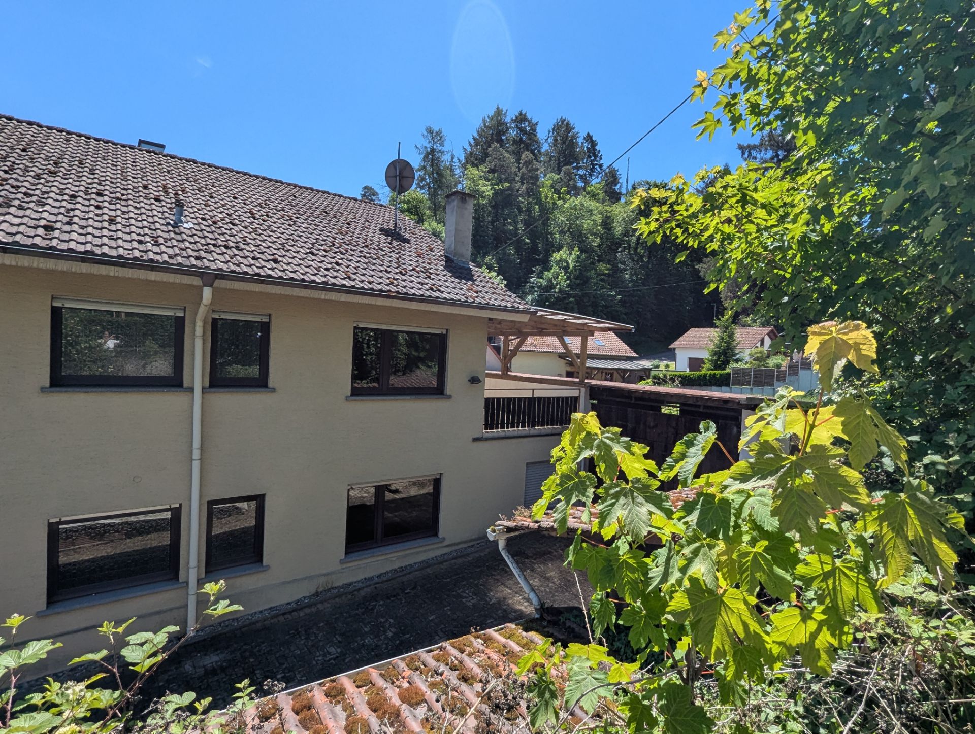 Zweistöckiges Wohnhaus mit mehreren Fenstern, dahinter Bäume und blauer Himmel.