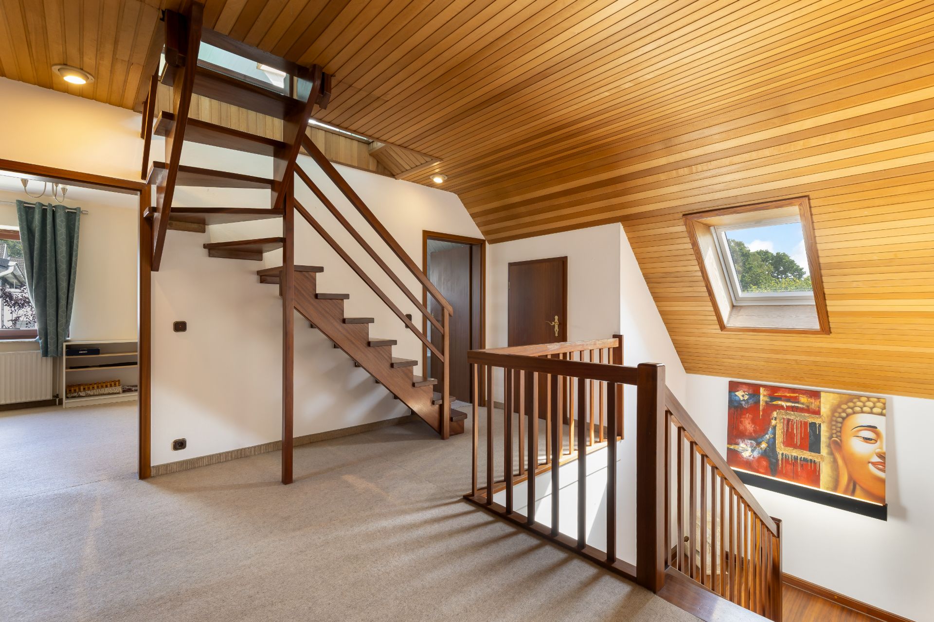 Helles Treppenhaus mit Holzdecken, Holztreppe, Fenster und Wandbild in einem Wohnhaus.