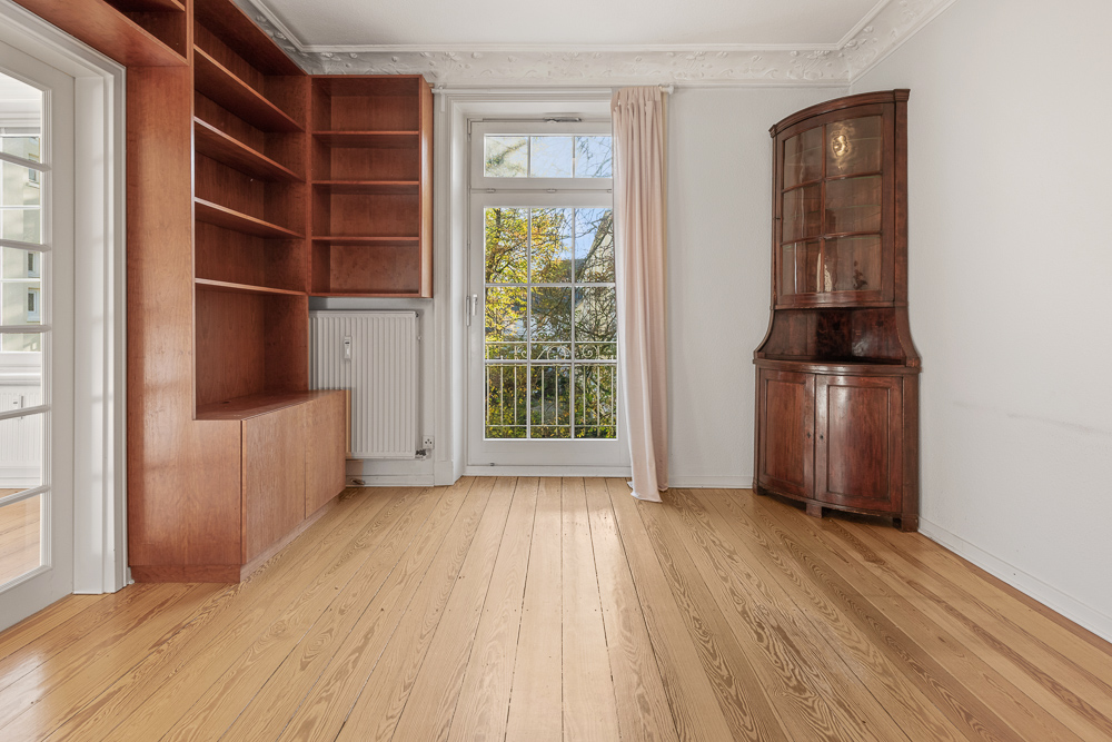 Zimmer mit Holzboden, Regalwand, Glastür, Fenster und Eckschrank.