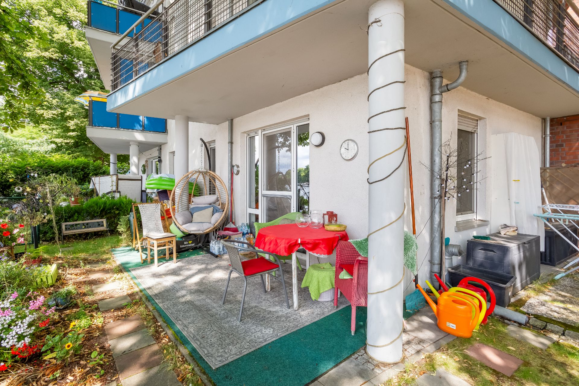 Überdachte Terrasse mit Tisch, Stühlen, Hängesessel und Garten neben einem Wohnhaus.