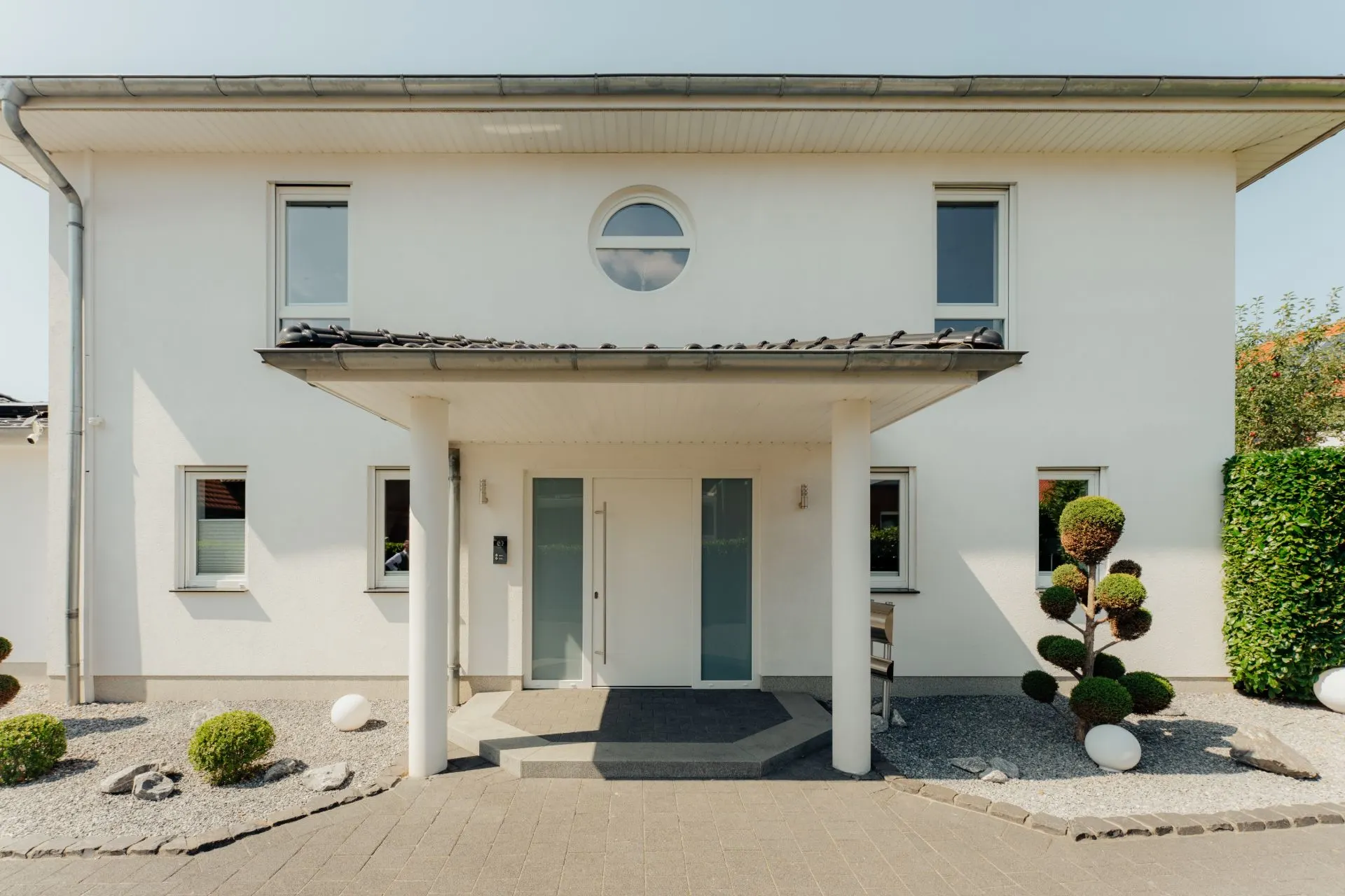 Moderne, weiß gestrichene Hausfassade mit symmetrischen Fenstern und gepflegtem Vorgarten.
