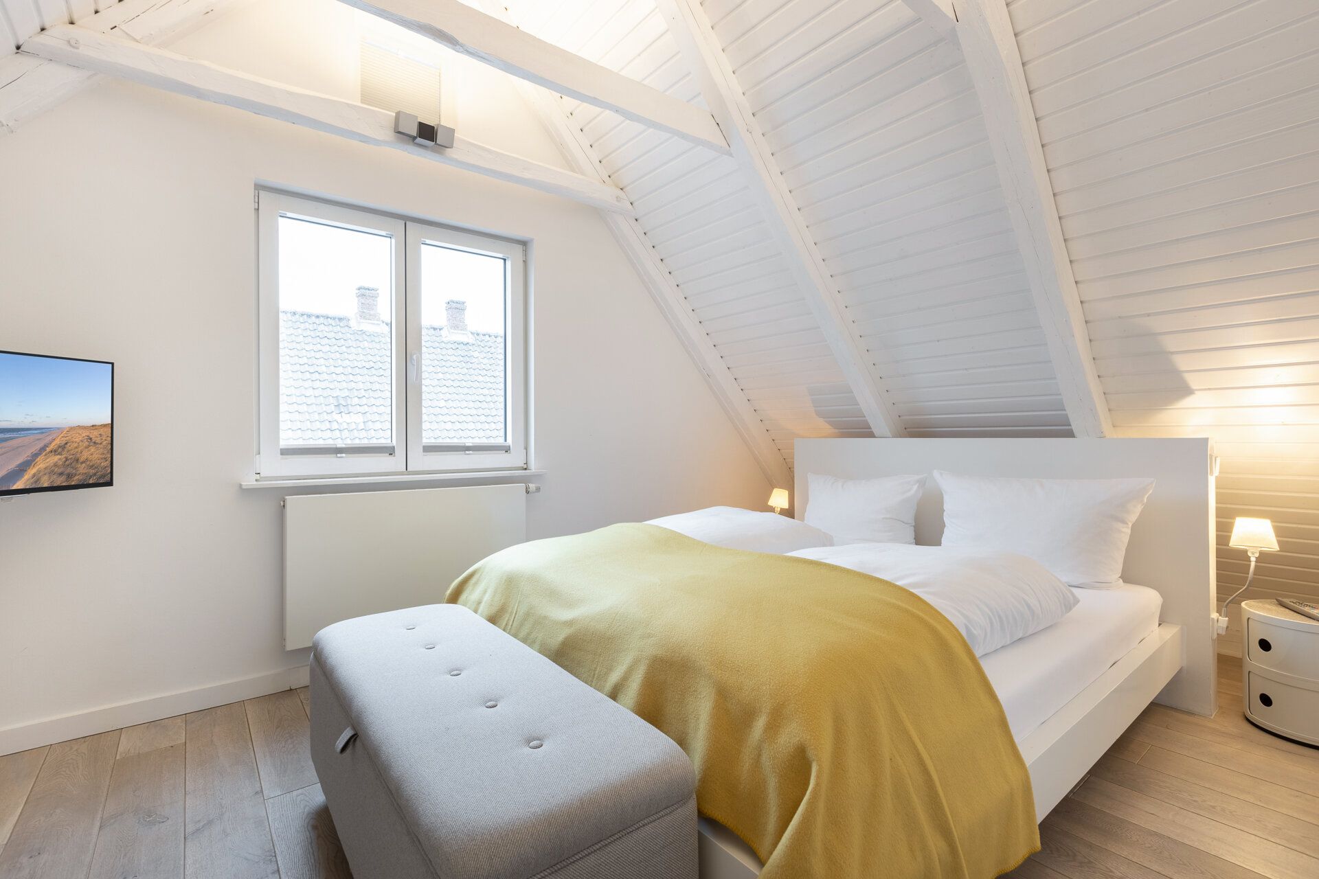 Helles Schlafzimmer mit Doppelbett, gelber Decke, Fernseher und Dachschrägen.