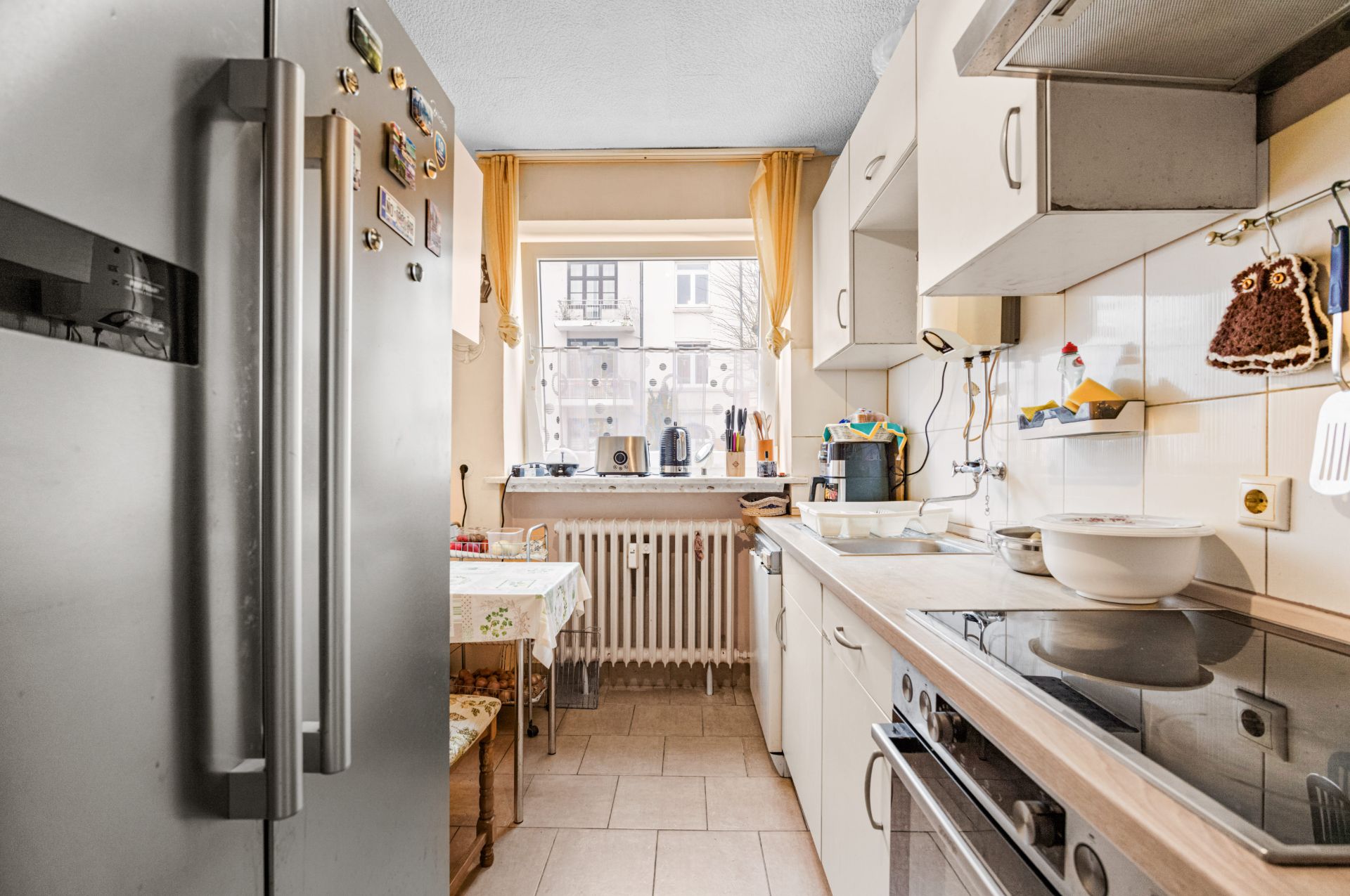 Helle Küche mit großem Kühlschrank, Herd, Spüle und Esstisch am Fenster.