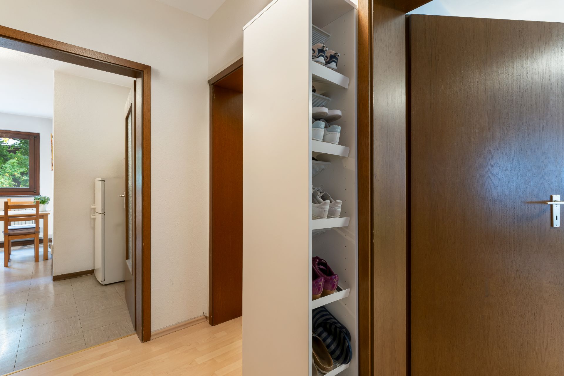 Flur mit offenem Schuhregal, Holztüren und Blick in eine Küche mit Esstisch.
